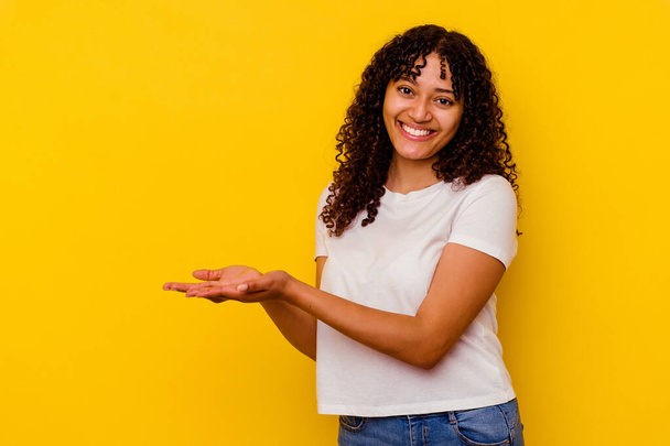 Young mixed race woman isolated on yellow background holding a copy space on a palm. - Photo, Image