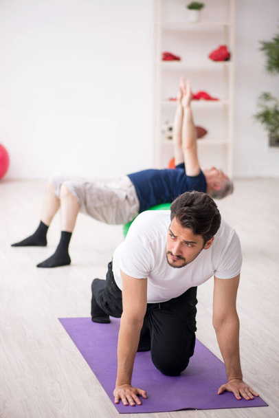 Young male instructor and old man doing sport exercises - Foto, immagini