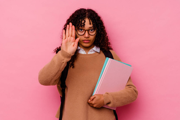 Молода студентка змішаної раси жінка ізольована на рожевому тлі, стоячи з простягнутою рукою, показуючи знак зупинки, запобігаючи вам
. - Фото, зображення