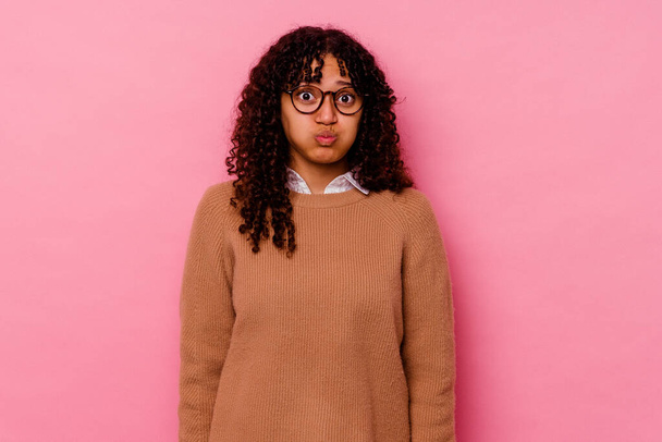 Young mixed race woman isolated on pink background blows cheeks, has tired expression. Facial expression concept. - Photo, Image