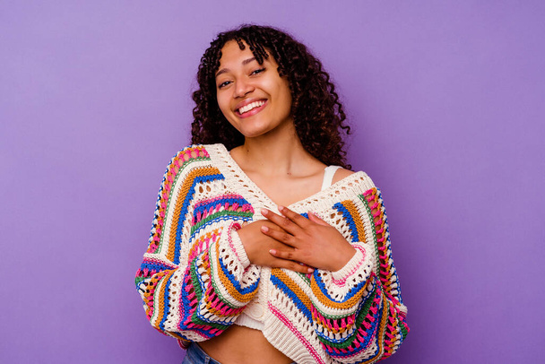 Young mixed race woman isolated on purple background has friendly expression, pressing palm to chest. Love concept. - 写真・画像