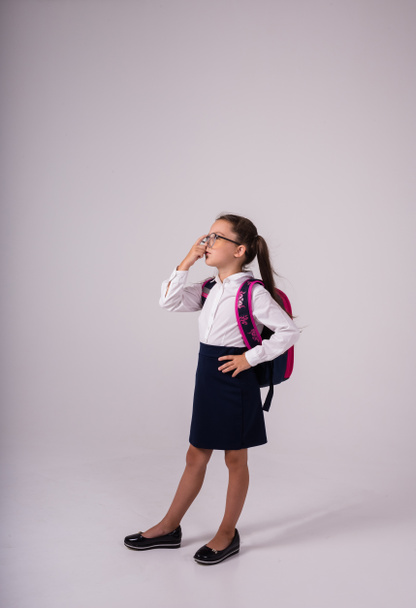 Умная школьница в форме в очках стоит на белом фоне с местом для текста - Фото, изображение