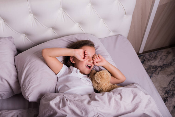 bambina bruna in pigiama si sveglia con sul letto in camera da letto - Foto, immagini
