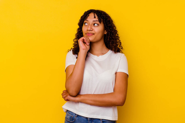 Young mixed race woman isolated on yellow background thinking and looking up, being reflective, contemplating, having a fantasy. - Foto, afbeelding