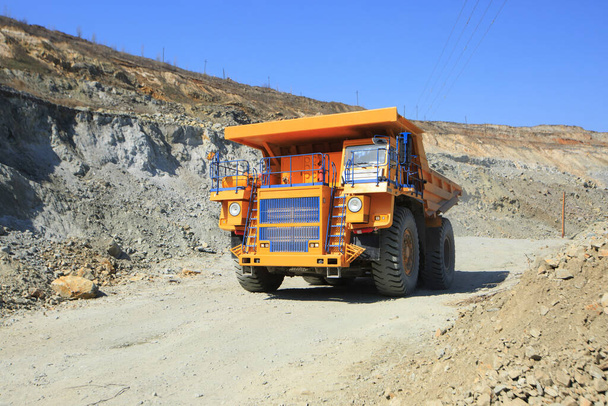 Gran camión de basura minera amarilla en la carretera en un día soleado. Equipos de gran tamaño para el transporte de masa de roca en una cantera de mineral. - Foto, imagen
