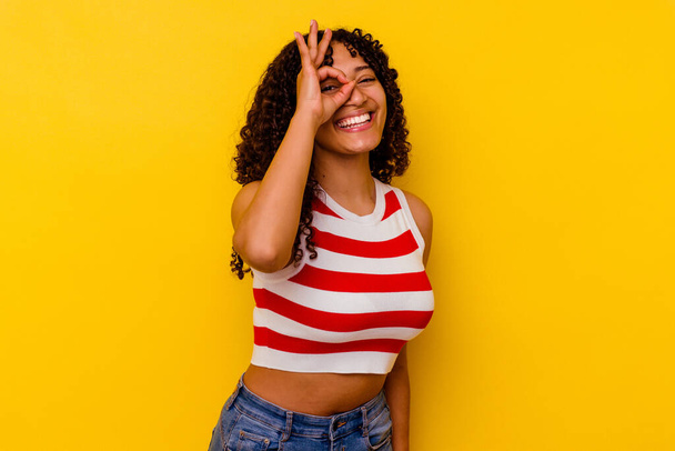 Young mixed race woman isolated on yellow background excited keeping ok gesture on eye. - Photo, Image