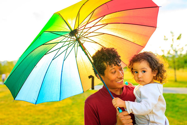 familia de raza mixta que cubre del sol bajo el paraguas brillante - Foto, imagen