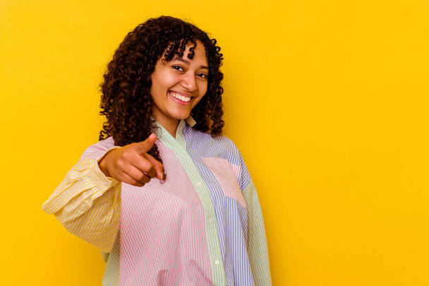 Mujer joven de raza mixta aislada sobre fondo amarillo apuntando hacia delante con los dedos. - Foto, Imagen