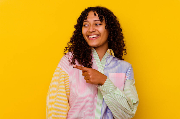 Mladá smíšená rasa žena izolované na žlutém pozadí vypadá stranou s úsměvem, veselý a příjemný. - Fotografie, Obrázek