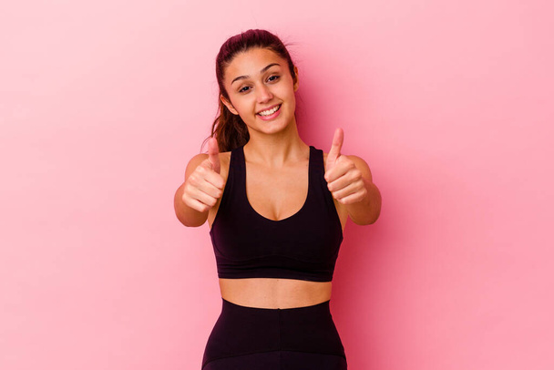 Young sport Indian woman isolated on pink background with thumbs ups, cheers about something, support and respect concept. - Foto, imagen
