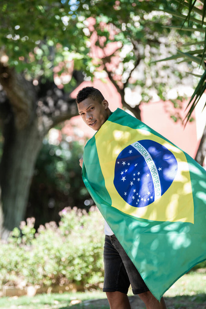 Latynos owinięty w brazylijską flagę patrzący w obiektyw: selektywna ostrość. Koncepcja różnorodności. - Zdjęcie, obraz