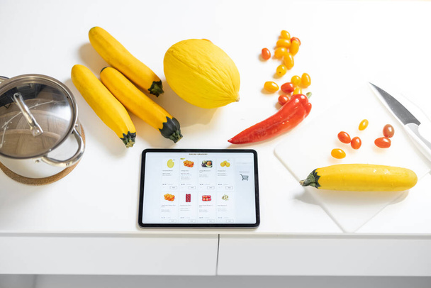 Świeże warzywa i stół cyfrowy z uruchomioną stroną internetową e-shop na białym stole - Zdjęcie, obraz