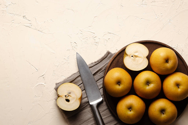Asian pears with a silver knife on a wooden plate and a brown piece of cloth, on a light background. - Foto, Imagen