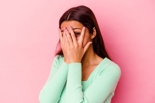 Young Indian woman isolated on pink background blink through fingers frightened and nervous. - Photo, Image