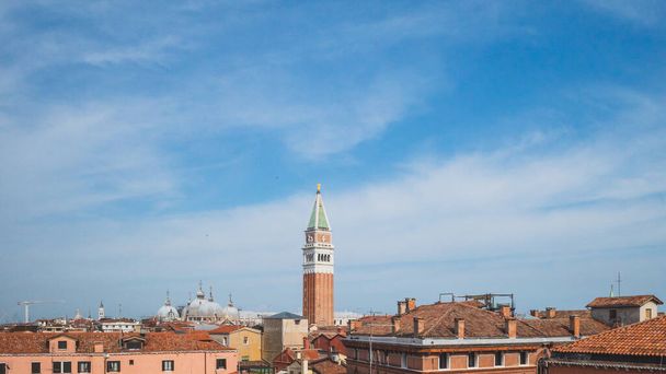 Näkymä San Marco kellotorniin perinteisten venetsialaisten talojen yllä sinisen taivaan alla Venetsiassa, Italiassa - Valokuva, kuva