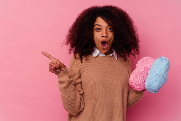 Young african american woman holding a sewing threads isolated on pink background pointing to the side - Photo, Image