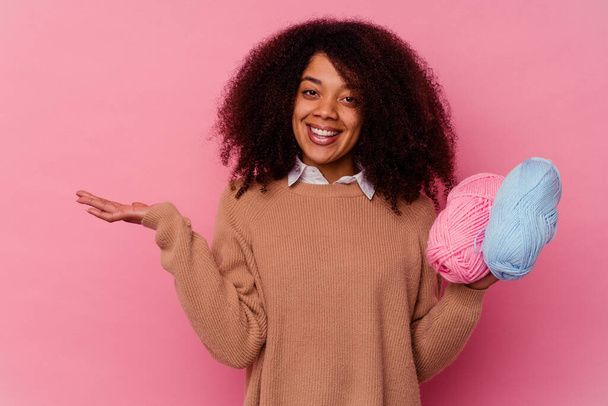 Giovane donna afroamericana che tiene un filo da cucito isolato su sfondo rosa mostrando uno spazio di copia su una palma e tenendo un'altra mano in vita. - Foto, immagini