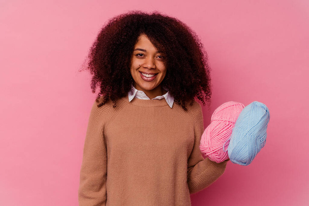 Jovem afro-americana segurando um fio de costura isolado no fundo rosa feliz, sorridente e alegre. - Foto, Imagem