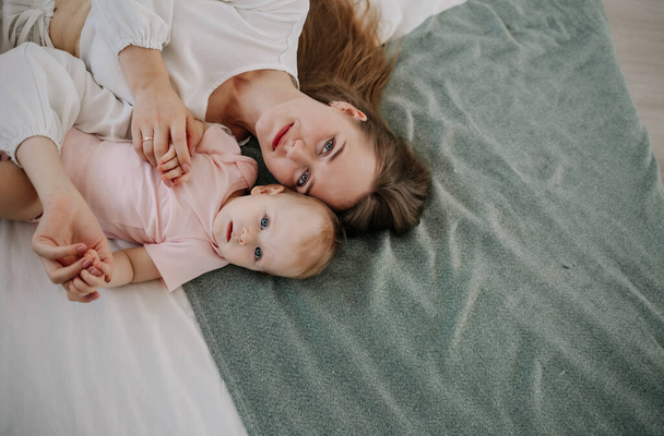a happy mother is lying with her baby daughter on the bed in the room. Top view - Foto, afbeelding