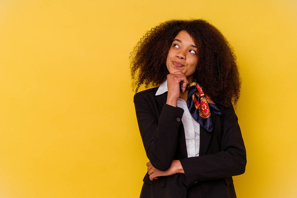 Giovane hostess aerea afroamericana isolata su sfondo giallo guardando lateralmente con espressione dubbia e scettica. - Foto, immagini