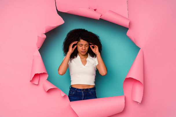 Junge Afroamerikanerin in zerrissenem Papier isoliert auf blauem Hintergrund berührt Schläfen und hat Kopfschmerzen. - Foto, Bild