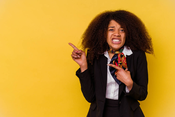 Junge afroamerikanische Stewardess isoliert auf gelbem Hintergrund schockiert und zeigt mit Zeigefinger auf einen Kopierraum. - Foto, Bild
