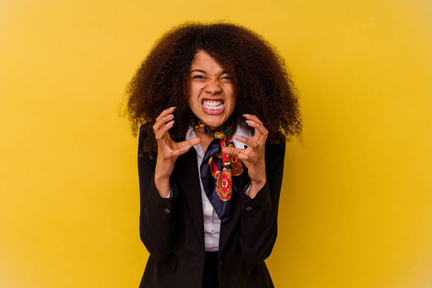 Young African American air hostess isolated on yellow background upset screaming with tense hands. - Photo, Image
