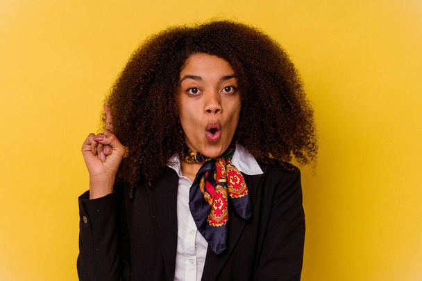 Jeune hôtesse de l'air afro-américaine isolée sur fond jaune ayant une bonne idée, concept de créativité. - Photo, image
