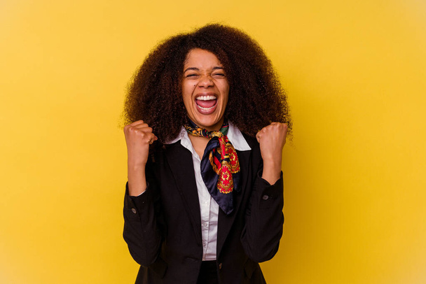 Jeune hôtesse de l'air afro-américaine isolée sur fond jaune acclamant insouciante et excitée. Concept de victoire. - Photo, image