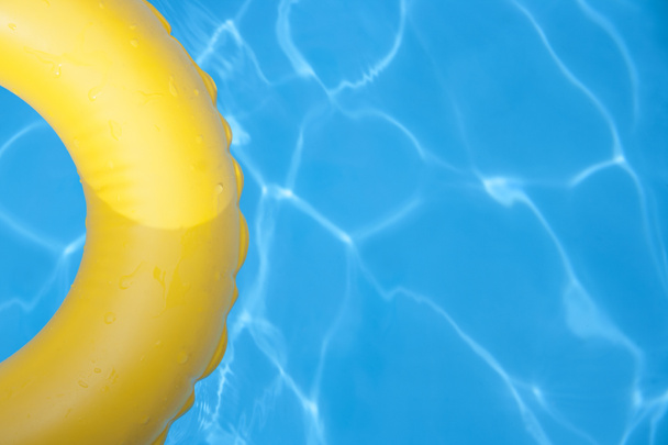 Detalle de anillo inflable amarillo flotando en piscina en día soleado. Vista superior. - Foto, Imagen