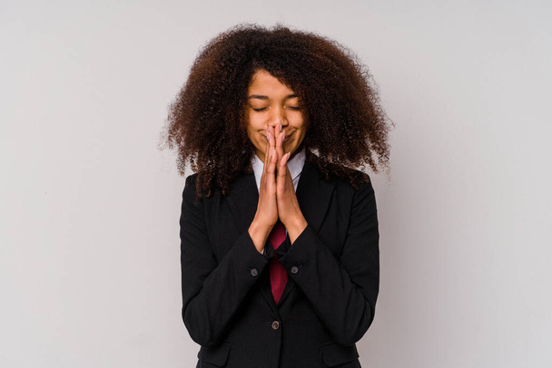 Młoda Afroamerykanka biznes kobieta w garniturze odizolowany na białym tle trzymając się za ręce w modlitwie blisko ust, czuje się pewnie. - Zdjęcie, obraz