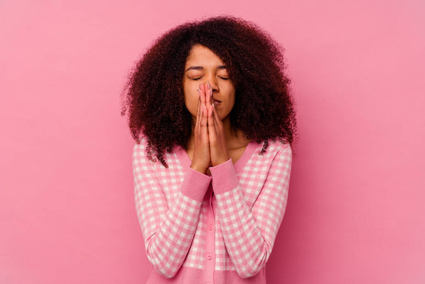 Νεαρή Αφροαμερικανή, απομονωμένη σε ροζ φόντο, να προσεύχεται κοντά στο στόμα, νιώθει σιγουριά.. - Φωτογραφία, εικόνα