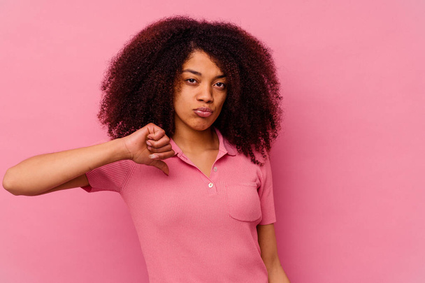 Νεαρή Αφρο-Αμερικανίδα, απομονωμένη σε ροζ φόντο, που δείχνει μια χειρονομία αντιπάθειας, κάτω οι αντίχειρες. Έννοια διαφωνίας. - Φωτογραφία, εικόνα