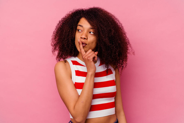Νεαρή Αφροαμερικανή, απομονωμένη σε ροζ φόντο, κρατώντας μυστικό ή ζητώντας σιωπή.. - Φωτογραφία, εικόνα