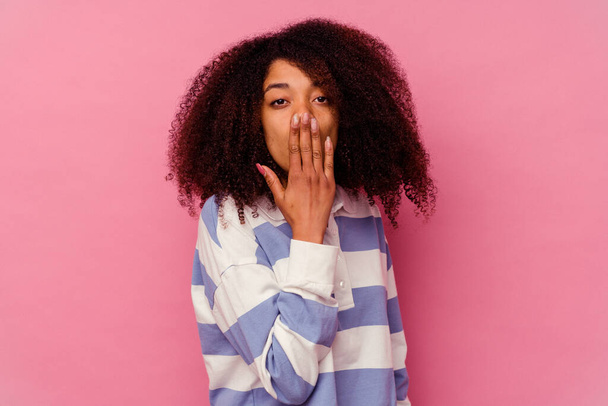 Νεαρή Αφροαμερικανή γυναίκα απομονωμένη σε ροζ φόντο σοκαρισμένη, που καλύπτει το στόμα με τα χέρια, ανυπομονεί να ανακαλύψει κάτι νέο.. - Φωτογραφία, εικόνα