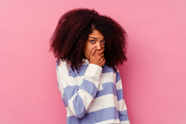 jong Afrikaans amerikaans vrouw geïsoleerd op roze achtergrond bedekking mond met handen kijken bezorgd. - Foto, afbeelding