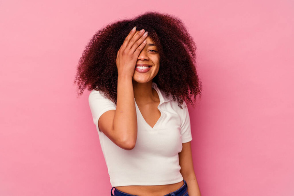 Young african american woman isolated on pink background having fun covering half of face with palm. - 写真・画像