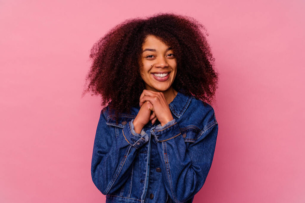 Young african american woman isolated on pink background keeps hands under chin, is looking happily aside. - Foto, Imagen