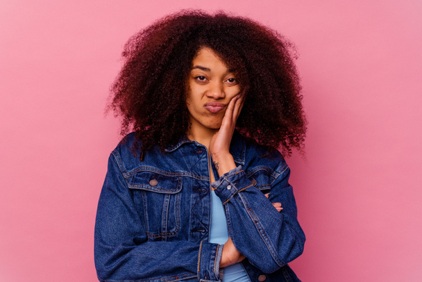Mujer afroamericana joven aislada sobre fondo rosa sopla mejillas, tiene expresión cansada. Concepto de expresión facial. - Foto, Imagen