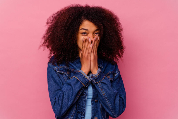 Молода афроамериканська жінка ізольована на рожевому фоні шокована, закриваючи рот руками, прагнучи знайти щось нове.. - Фото, зображення