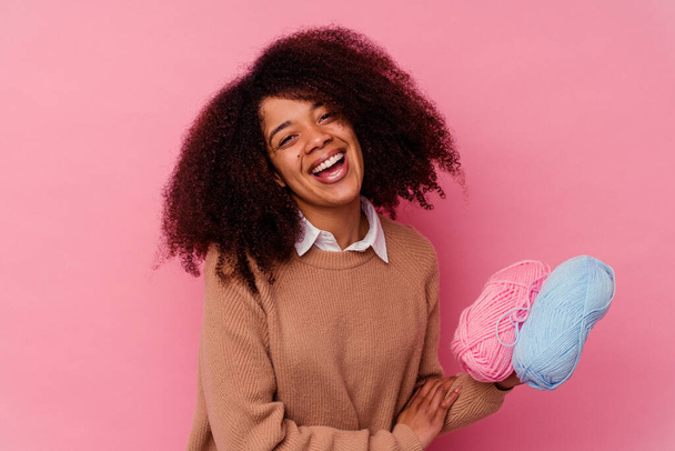 Junge afrikanisch-amerikanische Frau hält einen Nähfaden isoliert auf rosa Hintergrund, lacht und hat Spaß. - Foto, Bild