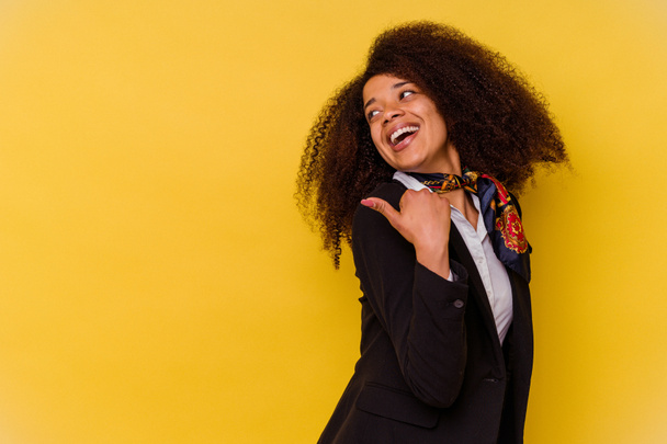 Young African American air hostess isolated on yellow background points with thumb finger away, laughing and carefree. - Foto, Imagem