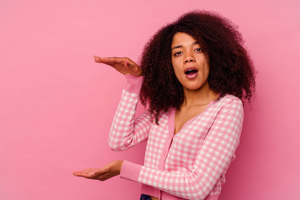 Fiatal afro-amerikai nő elszigetelt rózsaszín háttér megdöbbent és csodálkozott kezében egy másolási hely a kezek között. - Fotó, kép
