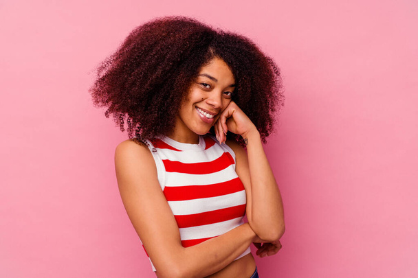 Νεαρή Αφροαμερικανή γυναίκα απομονωμένη σε ροζ φόντο χαμογελώντας χαρούμενη και με αυτοπεποίθηση, αγγίζοντας το πηγούνι με το χέρι. - Φωτογραφία, εικόνα