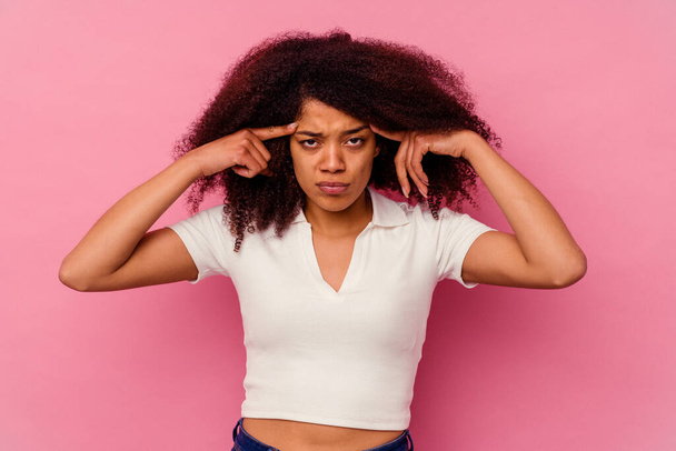 Young african american woman isolated on pink background focused on a task, keeping forefingers pointing head. - Photo, Image