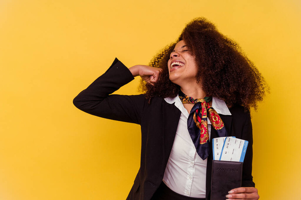 Giovane hostess aerea afroamericana in possesso di un biglietto aereo isolato su sfondo giallo alzando il pugno dopo una vittoria, concetto vincitore. - Foto, immagini