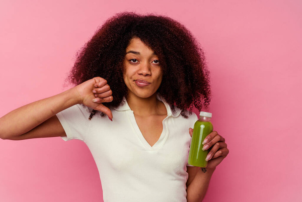 Mujer afroamericana joven bebiendo un batido saludable aislado sobre fondo rosa mostrando un gesto de aversión, pulgares hacia abajo. Concepto de desacuerdo. - Foto, Imagen