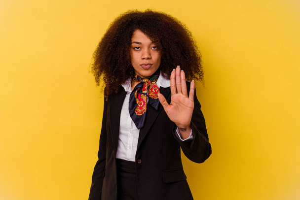 Jovem anfitriã aérea afro-americana isolada no fundo amarelo em pé com a mão estendida mostrando sinal de parada, impedindo-o. - Foto, Imagem
