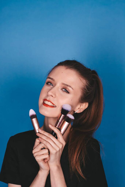  girl makeup artist with makeup brushes on a blue background. the brunette is thin. - Foto, afbeelding