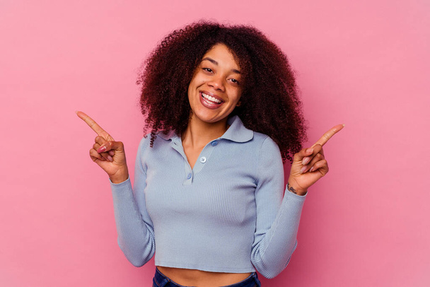 Young african american woman isolated on pink background pointing to different copy spaces, choosing one of them, showing with finger. - Foto, imagen